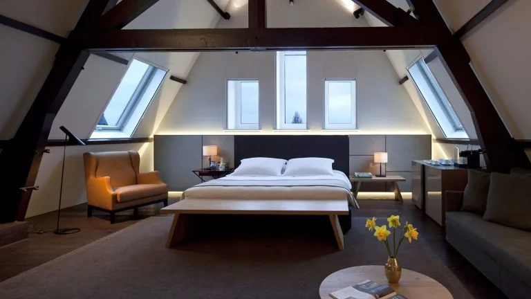 Luxe hotelsuite met bed en zithoek onder een groot dakraam.