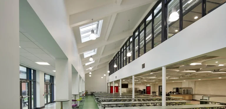 Ruime lichte schoolhal met hoge glaspartijen en daglicht van boven.
